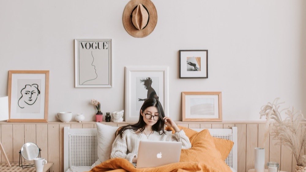 Woman lying on a bed with a laptop in a bedroom decorated with framed prints