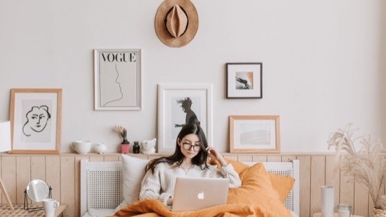 Woman lying on a bed with a laptop in a bedroom decorated with framed prints