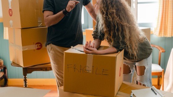 Man carrying a box marked fragile past a woman with curly hair