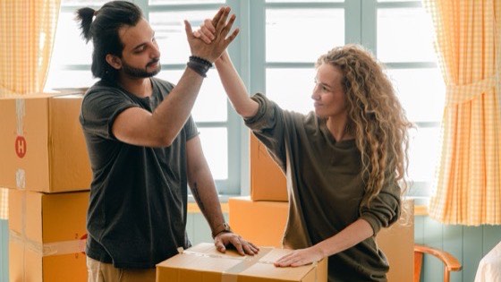 Couple high-fiving while packing boxes beside a window