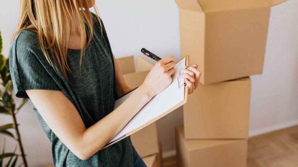 Woman filling in a checklist on a clipboard beside stacked cardboard boxes