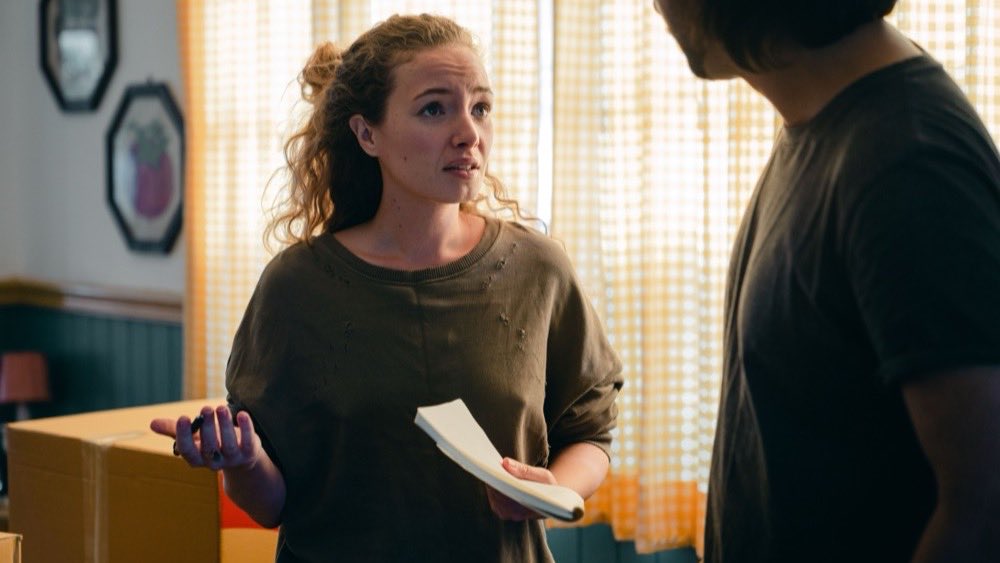 Woman holding papers mid-conversation with a man across a half-packed box