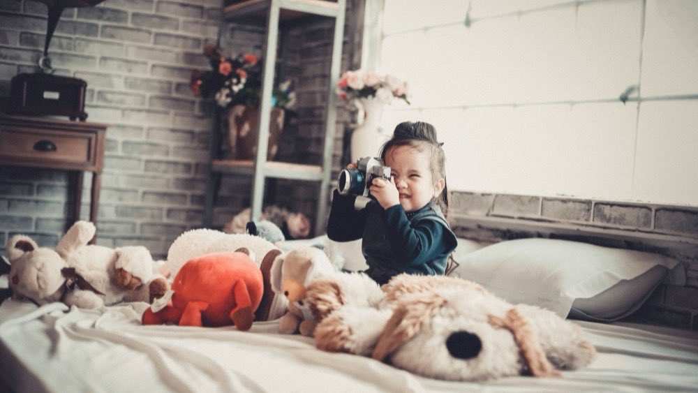 Toddler lying on a bed between two golden retrievers